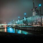 Night view of a modern building and waterfront with illuminated architecture and reflections.